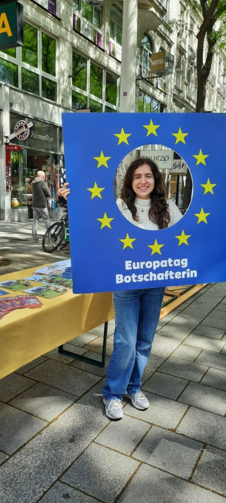 Eine Person schaut durch ein Bild mit Loch. Auf dem Bild steht "Europatag Botschafterin"