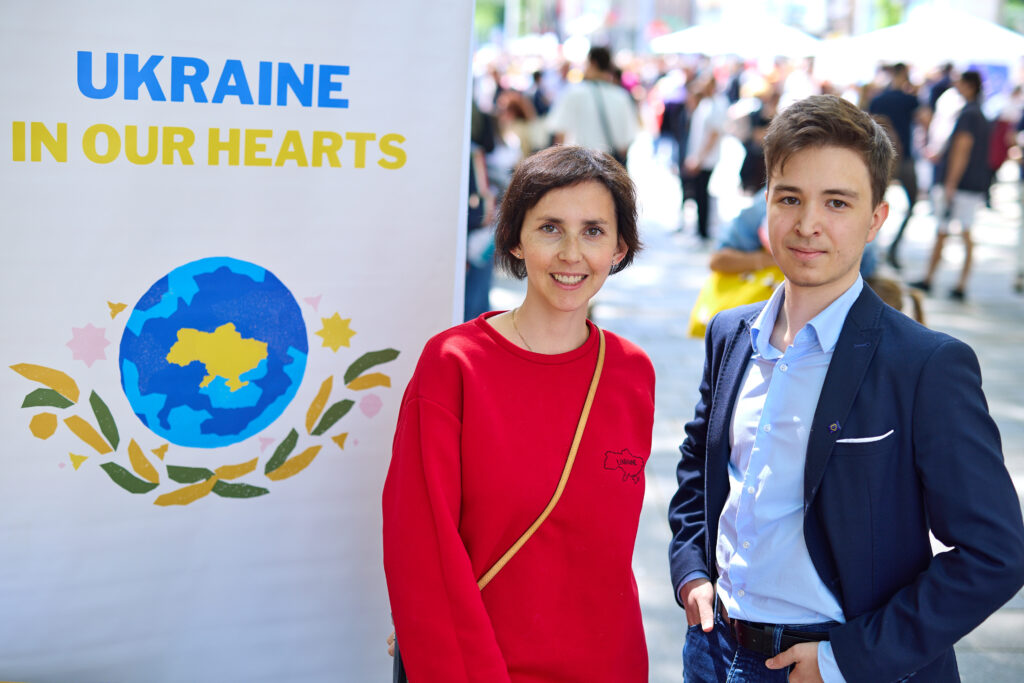 zwei Personen neben einem Rollup mit der Aufschrift "Ukraine in our Hearts"