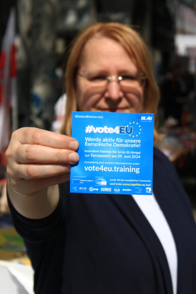eine Person hält einen Flyer in die Kamera