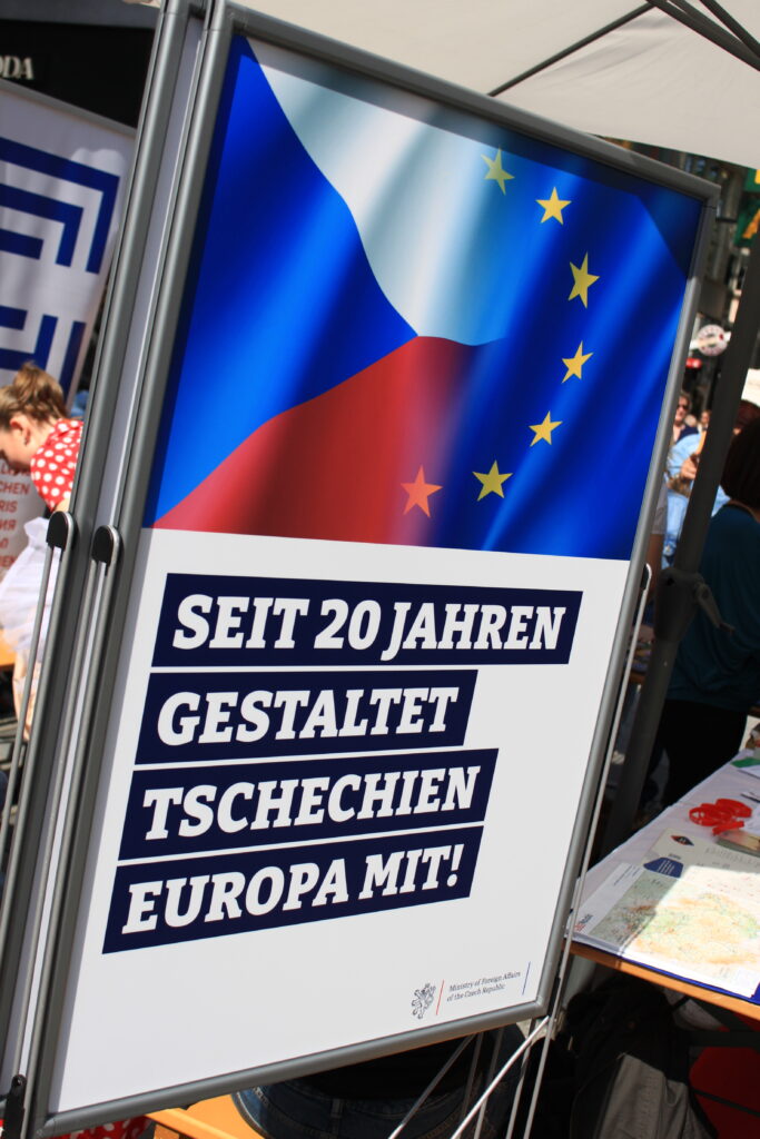 Ein Plakat: eine Flagge von Tschechien und die EU-Flagge miteinander verbunden. Text: Seit 20 Jahren gestaltet Tschechien Europa mit!