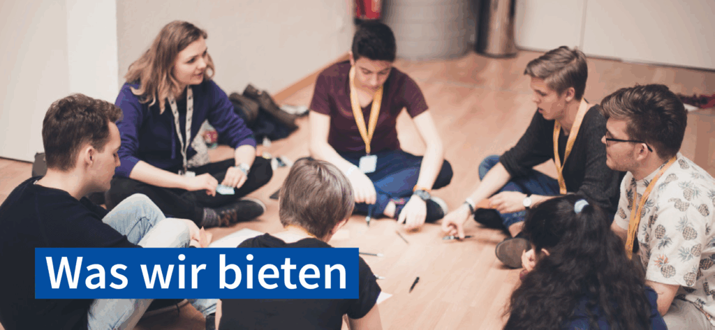 Farbfoto: 7 junge Menschen sitzen in einem Raum am Boden im Kreis und besprechen etwas. In der Mitte des Kreises sind Stifte und kleine Zettel zu sehen. Text: Was wir bieten
